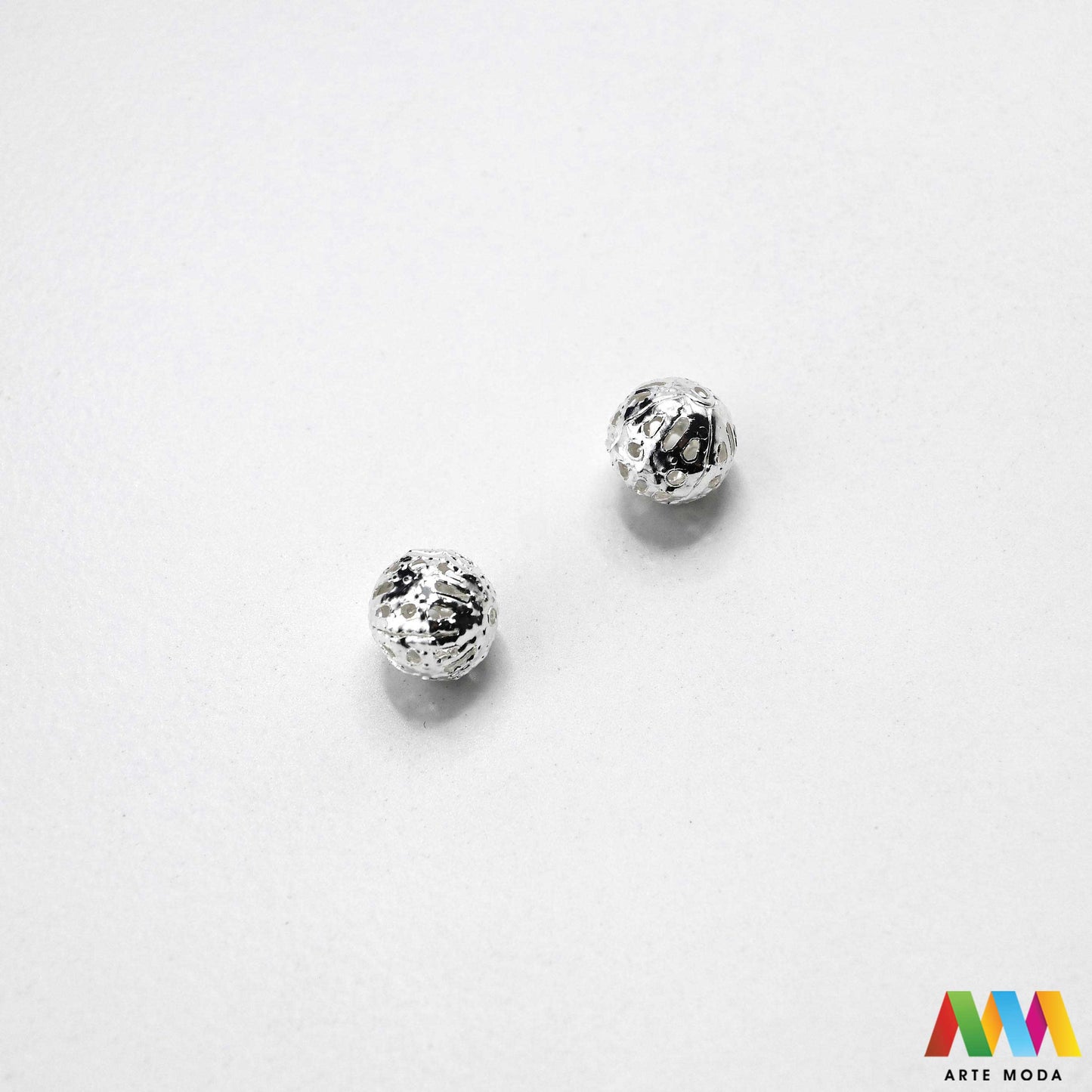 Elegantne metalne filigranske perle u srebrnoj, zlatnoj i nikal boji izložene na površini za izradu nakita. Prikazane su šupljikave i čipkaste metalne kuglice te ovalni filigranski distanceri s raznolikim vintage i orijentalnim uzorcima. Kvalitetan metalni repromaterijal i lagani razdjelnici s izbušenim rupama za provlačenje konca i igala, namijenjeni za izradu unikatnih narukvica, visećih naušnica i bogatih ogrlica u kreativnim DIY radionicama za izradu ručno rađenog modnog nakita arte moda repromaterijali